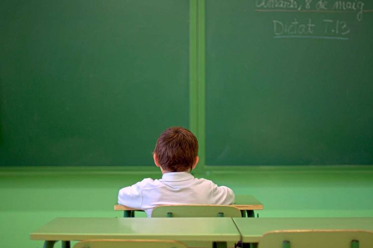 Ein Kind sitzt allein vor einer leeren Tafel.