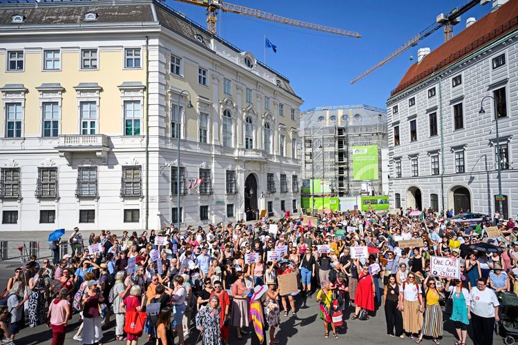 Große Menschenmenge bei einer Demonstration in Wien am 10. August 2026. Demonstrierende halten Plakate und Banner hoch, um auf die Forderungen des Aktionsbündnisses FRAUEN*Streiken aufmerksam zu machen. Im Hintergrund sind historische Gebäude, Baustellen und ein Kran zu sehen. Sonniges Wetter.