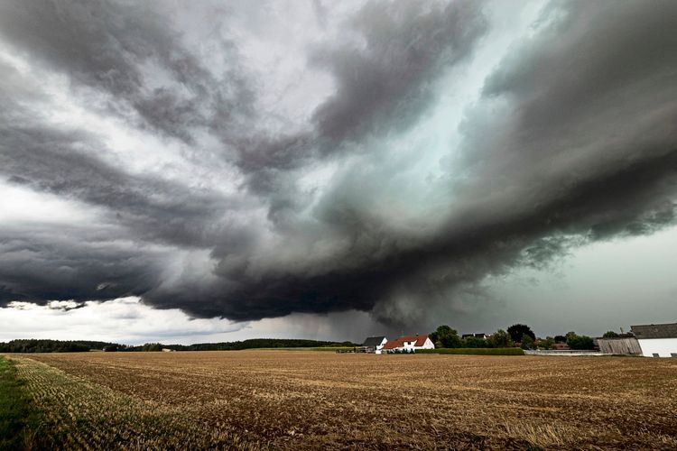 Bedrohlicher Himmel mit dunklen Gewitterwolken über einem Feld bei Ulm in Baden-Württemberg. Auffällige Strukturen linksausscherender Superzellen sorgen für eine dramatische Unwetterstimmung, im Hintergrund sind ein paar Häuser und Bäume erkennbar.