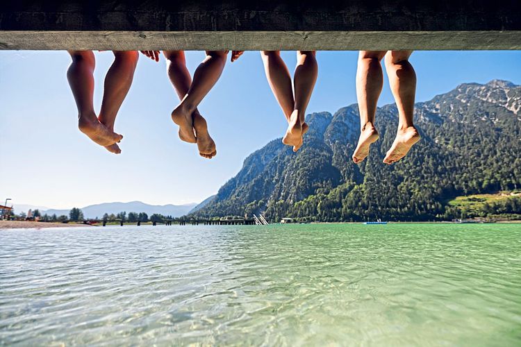 Bergsee in den österreichischen Alpen, Achensee, eine Familie lässt die Beine über der hellgrünen Wasseroberfläche sitzend von einem Pier baumeln.
