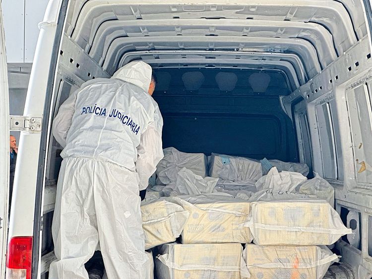 Drogen und andere Substanzen werden in weißen Verpackungen in einem Lastwagen gestapelt. Davor steht ein Polizist. Das Symbolbild stammt von einem Einsatz in Lissabon, Portugal.