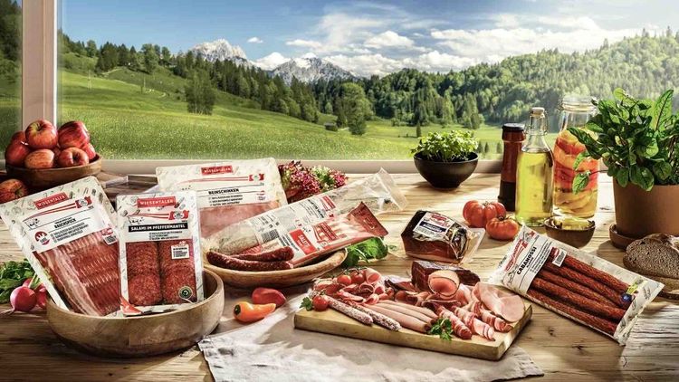Diverse verpackte Fleischprodukte, angerichtet vor einer grünen Landschaft