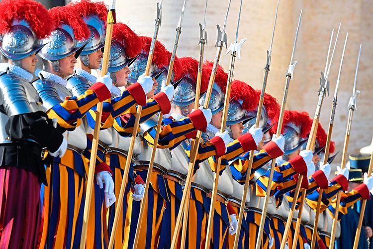 Schweizergardisten auf dem Petersplatz in Rom in ihren gelb-blau-roten Uniformen, mit Helmen und Harnischen und Hellebarden. 