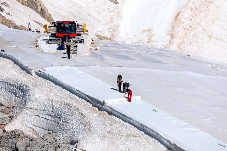 Menschen legen am Gletscher weiße Planen über dem Eis aus.