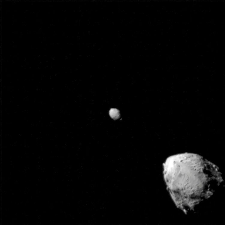 Schwarzweißaufnahme des Asteroiden Didymos (oben links) und seines Mondes Dimorphos (unten rechts) im Weltraum, aufgenommen etwa 2,5 Minuten vor dem Aufprall der NASA-DART-Raumsonde aus einer Entfernung von 920 Kilometern.