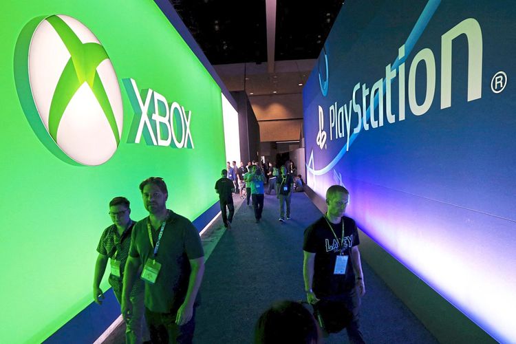 Besucher gehen auf der Electronic Entertainment Expo an einem Microsoft Xbox-Schild gegenüber einem Sony PlayStation-Schild vorbei