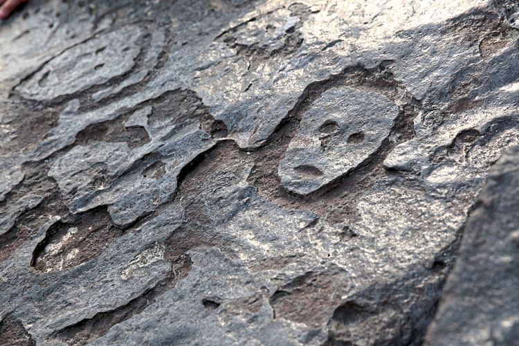 In schwarzen Fels sind Linien eingeritzt, die an einer Stelle den Umriss eines Gesichts mit Augen, Nase und Mund bilden.