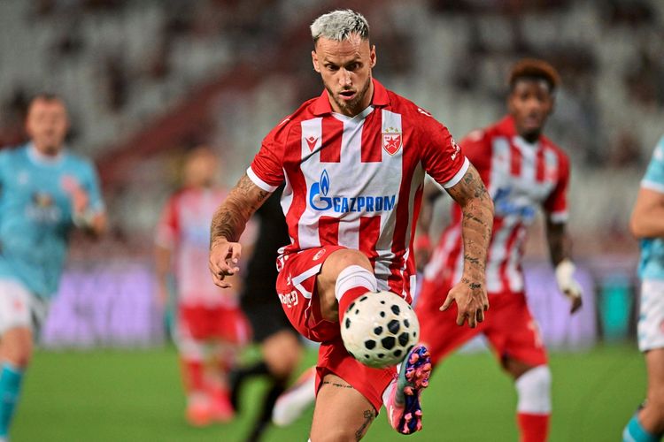 Ein Fußballspieler von Crvena Zvezda (Roter Stern Belgrad) in rot-weiß gestreiftem Trikot kontrolliert den Ball während eines Spiels gegen Larne aus Nordirland in der UEFA-Champions-League-Qualifikation im Rajko-Mitic-Stadion in Belgrad. Im Hintergrund sind weitere Spieler und unscharfe Zuschauer zu sehen.