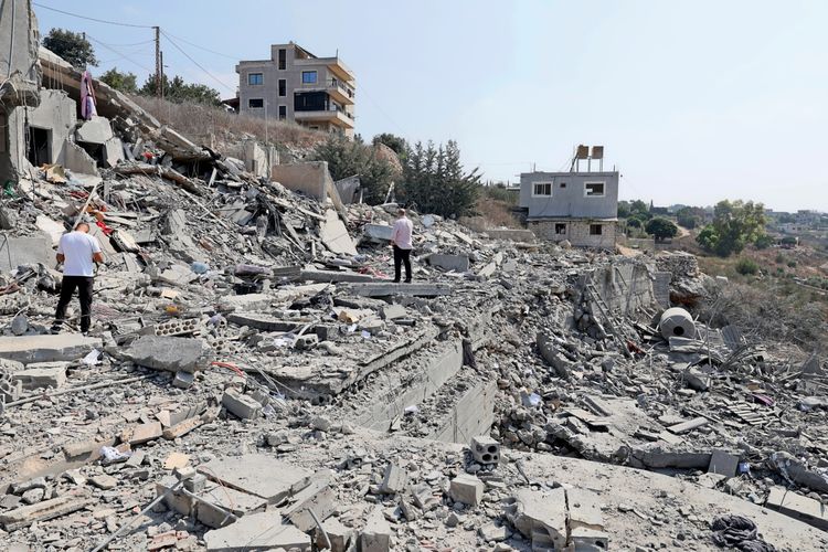 Zwei Personen stehen zwischen den Trümmern und inspizieren einen stark beschädigten Gebäudekomplex in der Ortschaft Ansar im Süden des Libanon, nach einem israelischen Luftangriff am 15. August 2026. Im Hintergrund sind intakte Gebäude und Bäume zu sehen.