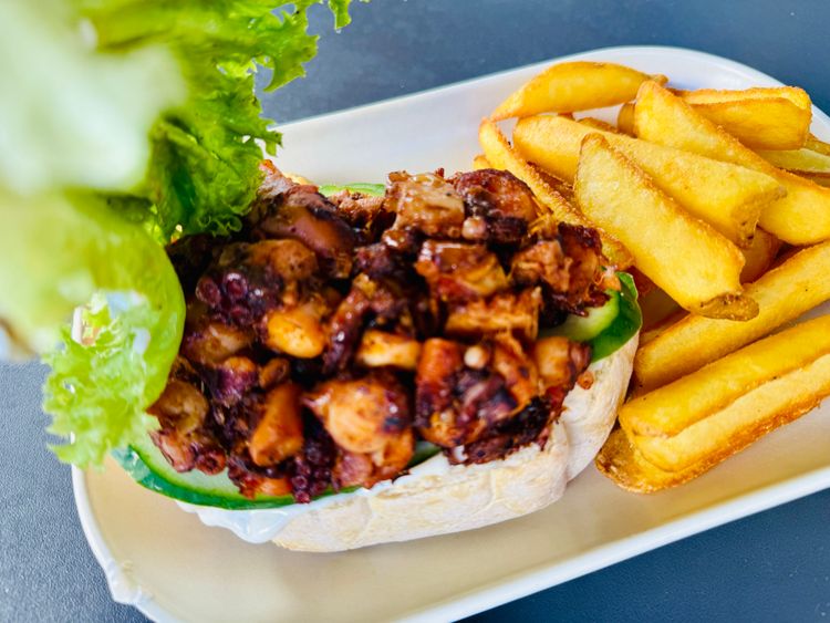 Weckerl, Salatblatt, Oktopus gegrillt und klein geschnitten, Pommes auf einem Teller