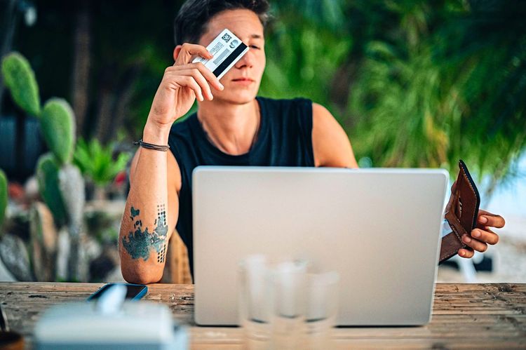 Junger Mann sitzt vor einem Notebook und bezahlt online mit Kreditkarte