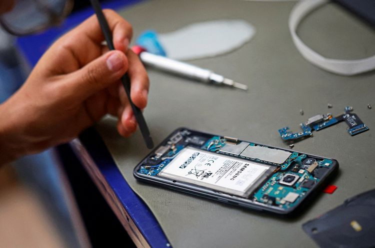 Eine Person repariert ein geöffnetes Samsung Galaxy S8 Smartphone, bei dem elektronischen Komponenten und die Batterie sichtbar sind. Auf einem Tisch liegen Werkzeuge und Bauteile.
