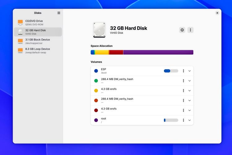 Screenshot des Linux-Laufwerksverwaltungswerkzeugs GNOME Disks in einem hellen App-Fenster vor blauem Hintergrund. In der linken Seitenleiste sind Laufwerke wie ein CD/DVD-Laufwerk, eine virtuelle 32-Gigabyte-Festplatte sowie Block- und Loop-Devices gelistet. Die Hauptansicht zeigt Details zur 32 GB großen VirtIO-Festplatte samt horizontalem, mehrfarbigem Speicherbelegungsbalken und einer Liste der darauf befindlichen Partitionen und Volumes, darunter ESP, DM-verity-Hashes, EROFS-Dateisysteme und eine Root-Partition.
