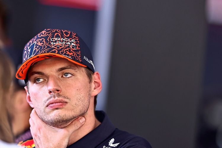 Verstappen schaut abwesend drein. Er trägt eine orange-blaue Kappe und hält sich die Hand an den Hals bzw. das Kinn.