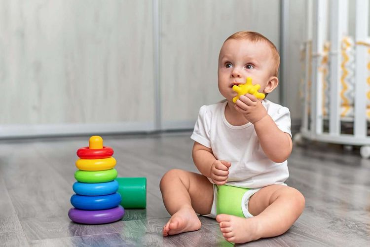 Baby sitzt am Boden und hat Spielzeug im Mund