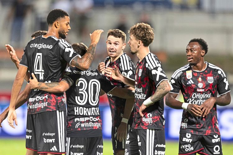 Eine Gruppe von LASK Linz-Spielern, darunter Spieler mit den Rückennummern 4 und 30, jubelt während eines Admiral Bundesliga-Spiels in Wolfsberg. Sie tragen schwarze Trikots mit roten und weißen Akzenten. Im Hintergrund ist ein unscharfer Stadionbereich zu sehen.
