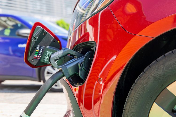Ein rotes Elektrofahrzeug, ein Mercedes EQV 300, wird an einer Ladestation in Ludwigshafen am Rhein aufgeladen. Im Hintergrund ist ein blaues Auto zu sehen.