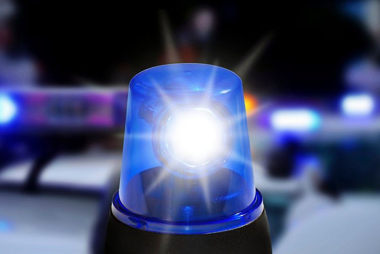 Nahaufnahme eines blau blinkenden Polizei-Blaulichts. Im Hintergrund sind verschwommene Notfalllichter und eine dunkle Szenerie zu erkennen.
