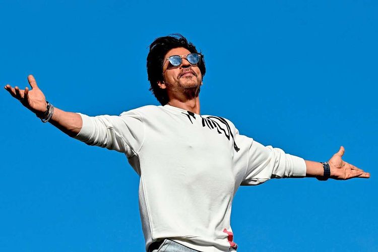 Shah Rukh Khan vor blauem Himmel mit ausgebreiteten Armen.