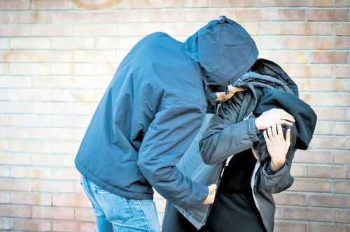 Ein junger Mann mit Kapuzenjacke attackiert einen anderen Jugendlichen, der schützend die Hände vor den Kopf hält