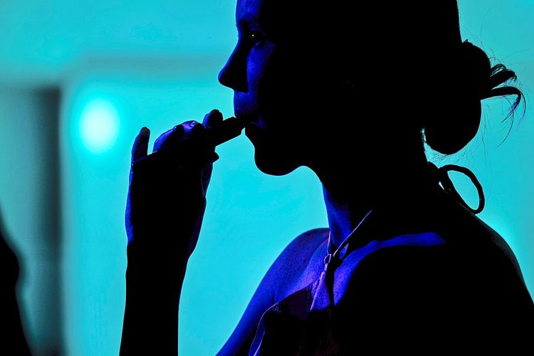 Silhouette einer Frau in blauem Licht, die an einer E-Zigarette zieht.