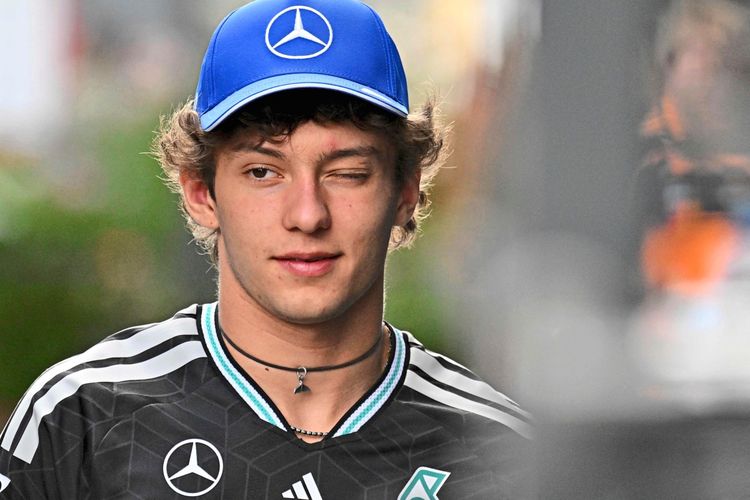 Ein junger Mann mit blauer Mercedes-Kappe und schwarzem Trikot geht im Fahrerlager. Hintergrund unscharf.