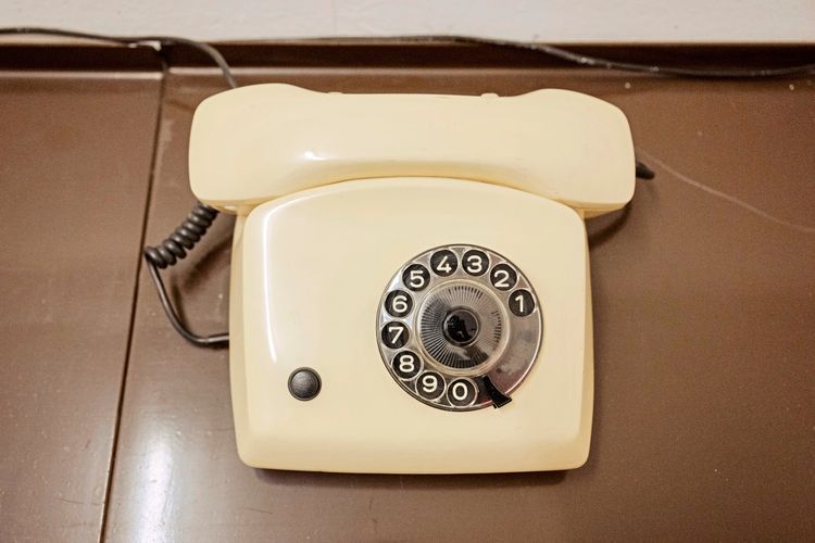 Ein cremefarbenes, altmodisches Telefon mit Wählscheibe auf einer braunen Oberfläche.