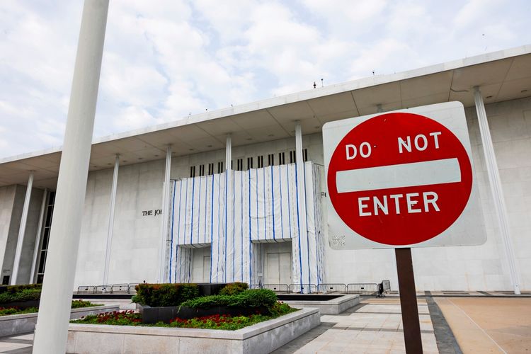 Das Bild zeigt die Vorderseite des John F. Kennedy Center for the Performing Arts in Washington, D.C., mit einem Baugerüst und einem verdeckten Bereich an der Fassade. Im Vordergrund steht ein „Do Not Enter“-Schild.