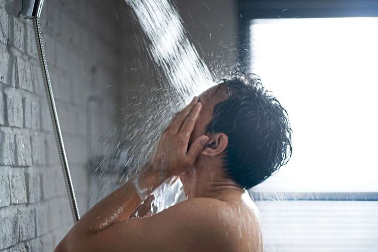 Mann steht in der Dusche, der Wasserstrahl geht auf sein Gesicht.