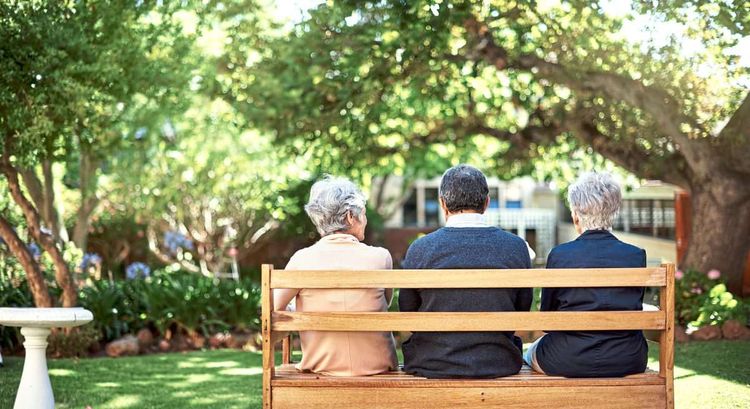 Drei Senioren sitzen auf einer Bank im Park, mit dem Rücken zum Betrachter
