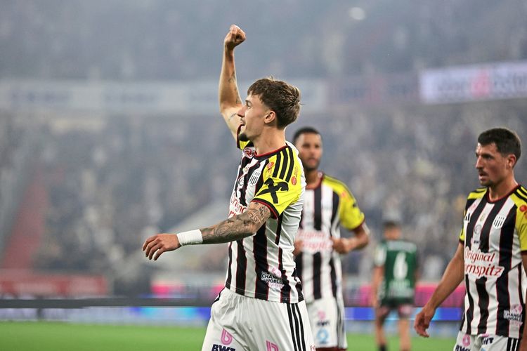 Ein Fußballspieler im gestreiften Trikot des LASK Linz jubelt mit erhobenem Arm über ein Tor während eines Spiels der Admiral Bundesliga gegen SV Oberbank Ried. Im Hintergrund sind weitere Spieler und unscharfe Zuschauer zu sehen.