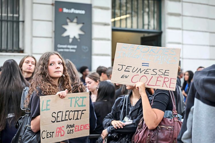 Eine Gruppe von Jugendlichen protestiert vor einem Gebäude. Zwei Personen halten Schilder hoch, auf denen Botschaften gegen Reformen und Ungleichheiten und für die Rechte der Schüler zu lesen sind. Im Hintergrund befinden sich weitere Demonstrierende.
