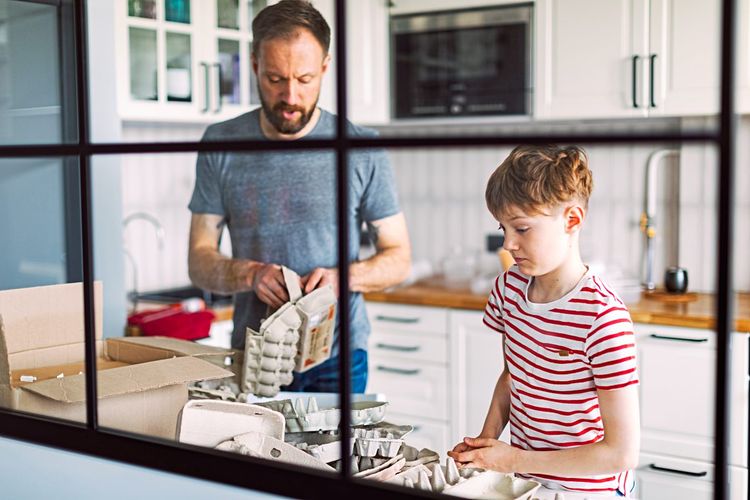 Papa und Sohn stehen in der Küche und sortieren Eierkartons