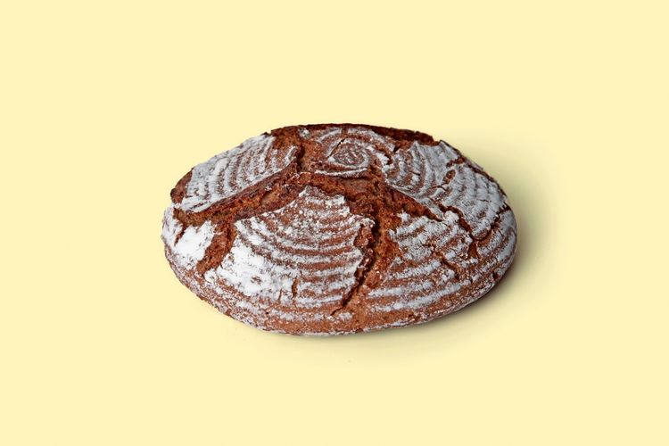 Ein rundes Roggenbrot mit rissiger Kruste und bemehlter Oberfläche, präsentiert vor einem hellgelben Hintergrund.