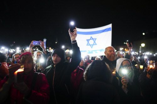 Menschen halten Lichter und Handys in die Höhe, im Hintergrund ist die Flagge Israels zu sehen.