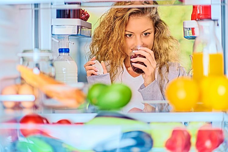 Frau steht vor offenem Kühlschrank und riecht an Lebensmittel