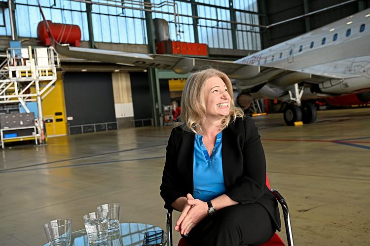 AUA-Chefin Annette Mann im Hangar am Flughafen Wien, vor einem AUA-Flieger an einem Tischchen sitzend.