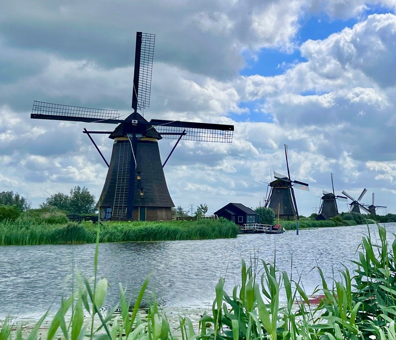 Mehrere Windmühlen vor wolkenverhangenem Himmel und Wasserstraße