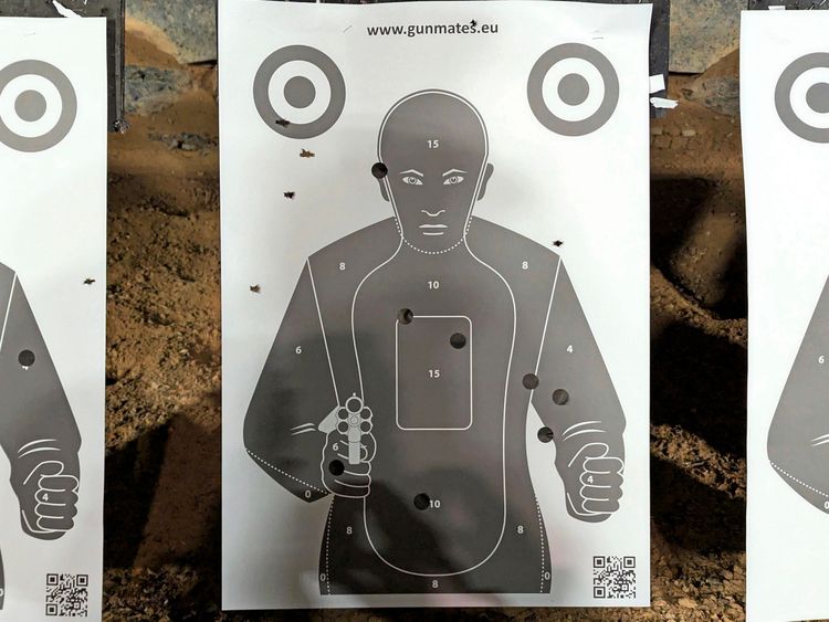 Zielscheibe mit der Silhouette einer Person, auf die mehrere Treffer abgegeben wurden. Die Trefferpunkte sind auf verschiedene Bereiche der Figur verteilt, insbesondere im Torso- und Arm-Bereich. Oben und unten auf dem Blatt sind QR-Codes sichtbar.