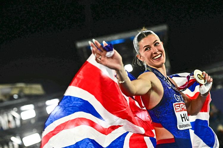 Eine britische Athletin feiert mit der Landesflagge und einer Goldmedaille bei den Leichtathletik-Europameisterschaften im Alexander Stadium in Birmingham am 10. August 2026. Sie lächelt und winkt jubelnd.