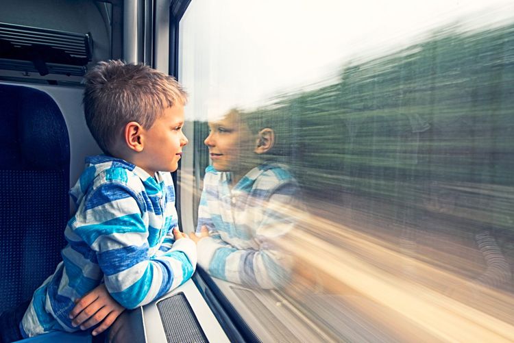 Kleiner Junge im Alter von 6 Jahren reist im Zug. Er lächelt und schaut aus dem Fenster.