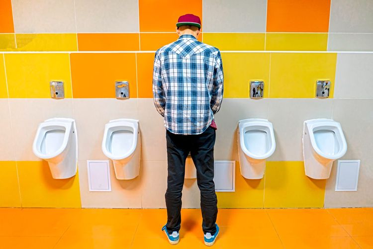 Mann steht vor einem Pissoir in einer öffentlichen Toilette