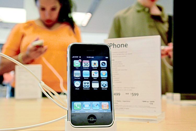 Ein iPhone ist in einem Geschäft ausgestellt. Dahinter eine Kundin, die auf ein Handy schaut.