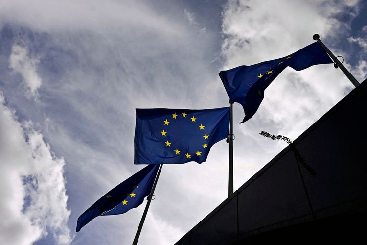 Drei europäische Flaggen wehen vor dem Berlaymont-Gebäude, dem Hauptsitz der Europäischen Kommission, in Brüssel vor einem bewölkten Himmel.