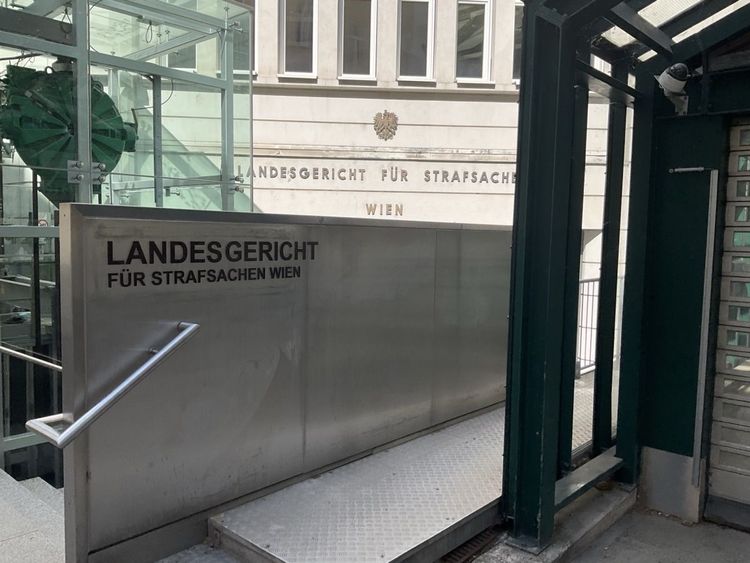 Eingangsbereich des Landesgerichts für Strafsachen Wien. Im Vordergrund eine Rampe mit Handlauf, im Hintergrund die Gebäudefassade mit dem Schriftzug und dem österreichischen Wappen.