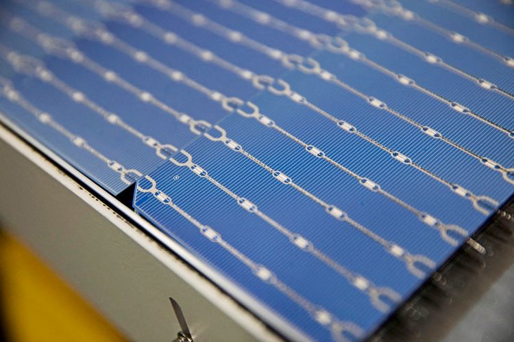 Nahaufnahme einer blauen Solarzelle mit sichtbaren silbernen Leiterbahnen in einer Fabrik.