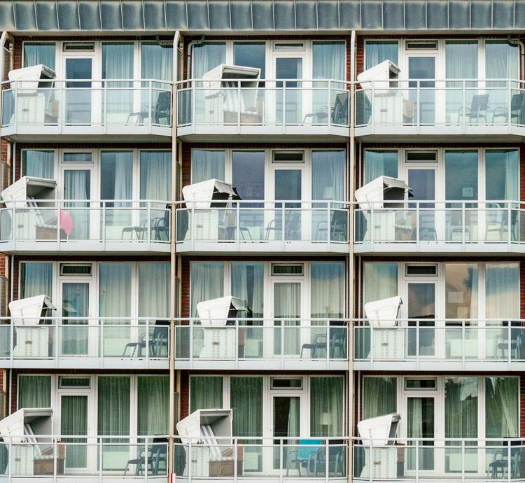 Mehrstöckiges Gebäude mit Balkonen, auf denen jeweils Strandkörbe stehen. Große Fenster mit Vorhängen sind in den Ferienwohnungen sichtbar.