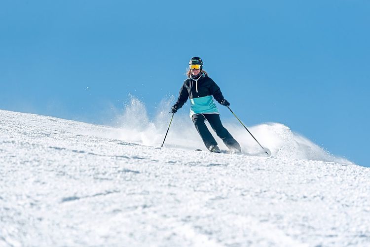 Frau fährt auf Skiern eine Piste hinunter, hinter ihr strahlend blauer Himmel