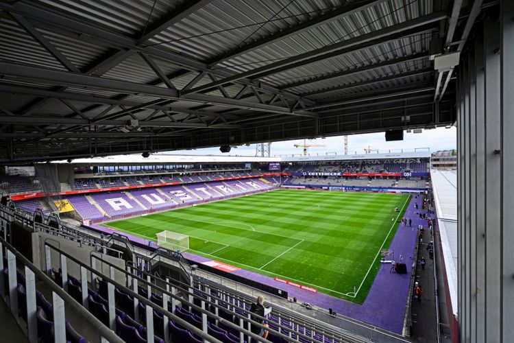 Blick auf das leere Fußballstadion Generali Arena in Wien, mit gut gepflegtem Rasen und lilafarbenen Sitzplätzen. Im Hintergrund sind Baukräne und eine überdachte Tribüne sichtbar.