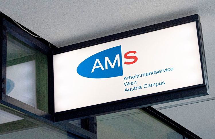 Ein Schild hängt an einem Gebäude. Oben steht: AMS - Arbeitsmarktservice Wien Austria Campus.